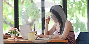 Young Asian woman is using a computer laptop while sitting at the wooden working desk