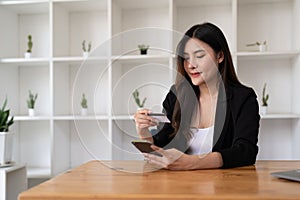 Young Asian woman using credit card and mobile phone for online shopping in coffee shop or coworking space, coffee cup