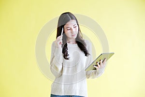 Young asian woman using digital tablet while standing over isolated yellow background