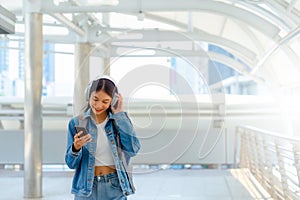 Young asian woman using headphone for listening nice music and walking in city