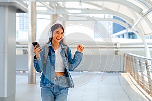 Young asian woman using headphone for listening nice music and walking in city