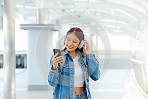 Young asian woman using headphone for listening nice music and walking in city. Girl happiness