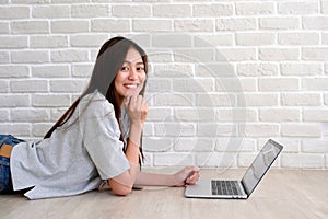 Young asian woman using laptop computer in front of white brick wall background with copy space, people and technology, lifestyles