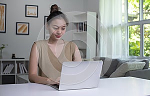 Asian woman using laptop at home, looking at screen, chatting, reading or writing email, sitting on desk