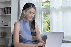 Young Asian woman using laptop at home, looking at screen, chatting, reading or writing email, sitting on desk