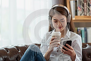 Young Asian woman using mobile phone and holding a hot cup of coffee, happy and relaxing time