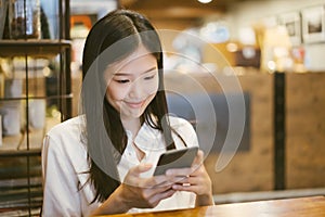 Young Asian woman using phone at a coffee shop happy and smile.