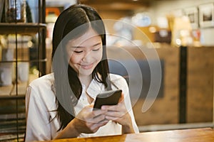 Young Asian woman using phone at a coffee shop happy and smile.