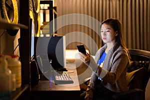Young Asian woman using phone while working overtime at home
