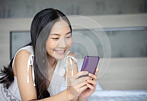 Young Asian woman using smart phone in bedroom happy and smile.