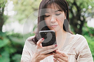 Young Asian woman using smart phone for chating or seaching information. A woman with smiley face in greeny garden. Digital