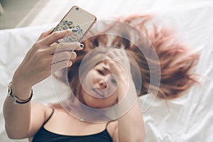 Young Asian woman using smart phone taking selfie picture. Woman lying on bed holding smart phone