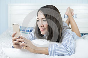 Young asian woman using smartphone while laying on the bed.