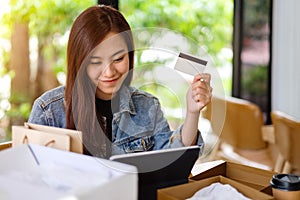 A young asian woman using tablet pc and credit card for online shopping with postal parcel box and shopping bags
