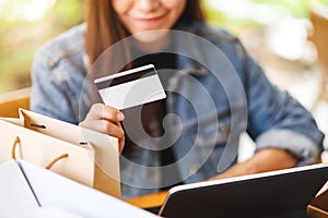 A young asian woman using tablet pc and credit card for online shopping with postal parcel box and shopping bags