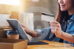 A young asian woman using tablet pc and credit card for online shopping with postal parcel box and shopping bags