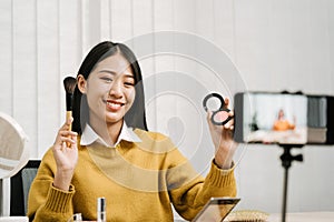 Young asian woman vlogging herself about beauty products with making a video for her blog on cosmetics using phone camera at home