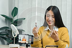 Young asian woman vlogging herself about beauty products with making a video for her blog on cosmetics using phone camera at home