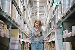 Young asian woman walking around a furniture warehouse store and looking a smartphone.