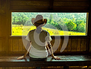 Young Asian woman wear the hat sit on wooden bench and watching beautiful view of green grass field and forest photo