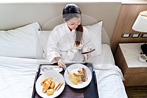 Young Asian woman wearing bathrobe enjoy breakfast on a bed in bedroom
