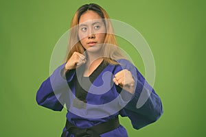 Young Asian woman wearing blue karate Gi against green background