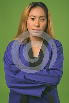 Young Asian woman wearing blue karate Gi against green background