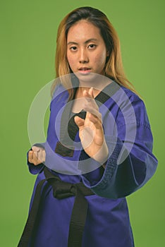 Young Asian woman wearing blue karate Gi against green background