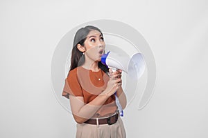 Young Asian woman wearing a brown shirt feeling surprised while shouting and screaming loud using megaphone speaker. Communication