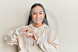 Young asian woman wearing casual sweatshirt smiling in love doing heart symbol shape with hands