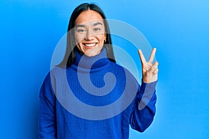 Young asian woman wearing casual winter sweater showing and pointing up with fingers number two while smiling confident and happy