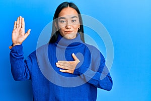 Young asian woman wearing casual winter sweater swearing with hand on chest and open palm, making a loyalty promise oath