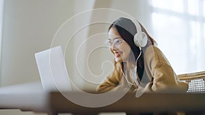 Young asian woman wearing glasses and headset working on computer laptop at house