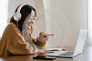 Young asian woman wearing glasses and headset working on computer laptop at house