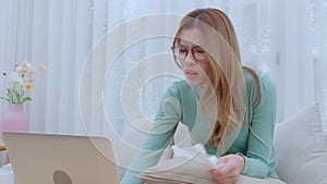 Young asian woman wearing glasses sitting on sofa worried with bills about financial and stress at home.