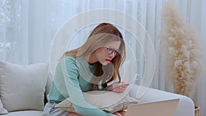 Young asian woman wearing glasses sitting on sofa worried with bills about financial and stress at home.
