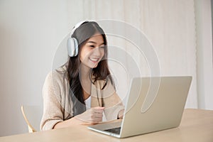 Young asian woman wearing headset while working on computer laptop at house