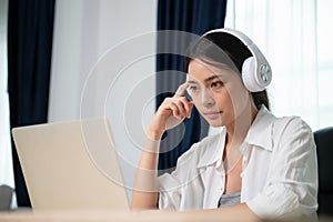 Young asian woman wearing headset working on computer laptop at house