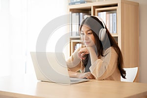 Young asian woman wearing headset while working on computer laptop at house