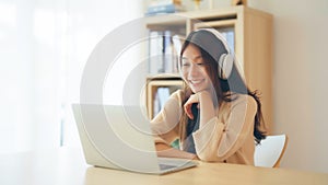 Young asian woman wearing headset while working on computer laptop at house