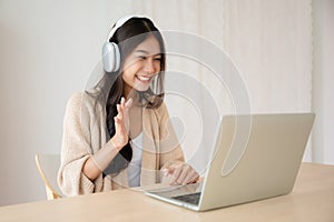 Young asian woman wearing headset while working on computer laptop at house