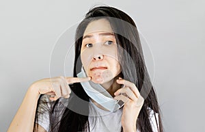 Young asian woman wearing medical face mask and white t shirt, her hand point at pimple on chin,Skin allergy From wearing a mask