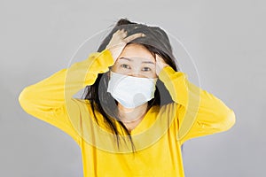 Young Asian woman wearing medical face mask and yellow shirt her hand on the head. isolated on gray background,health care concept