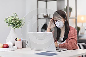 Young Asian woman wearing medical mask working on laptop during remotely work at home