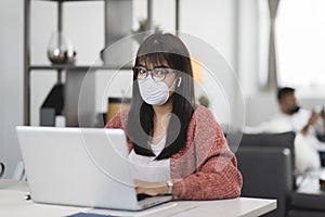 Young Asian woman wearing medical mask working on laptop during remotely work at home.