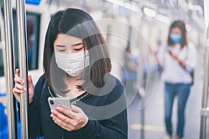 Young asian woman wearing protective face mask using smartphone in underground train due to the polluted air or pm 2.5 and