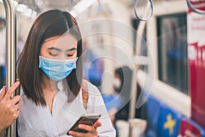 Young asian woman wearing protective face mask using smartphone in underground train due to the polluted air or pm 2.5 and