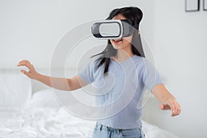 Young asian woman wearing vr headset playing game with excited in the bedroom at home.