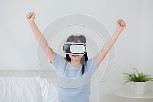 Young asian woman wearing vr headset playing game with excited in the bedroom at home.