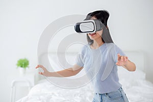 Young asian woman wearing vr headset playing game with excited in the bedroom at home.